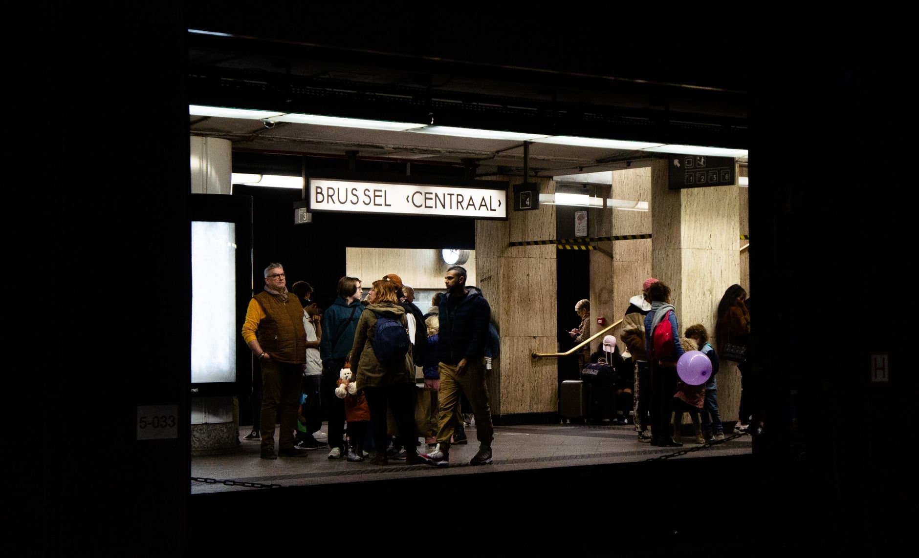 Group of people waiting at Brussels Centraal train station platform at night.
